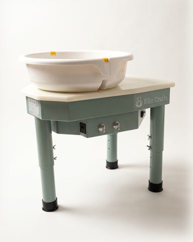 The Kiln Crafts Daisy pottery wheel in sage green with a cream wipe-clean top and push-button splash pan