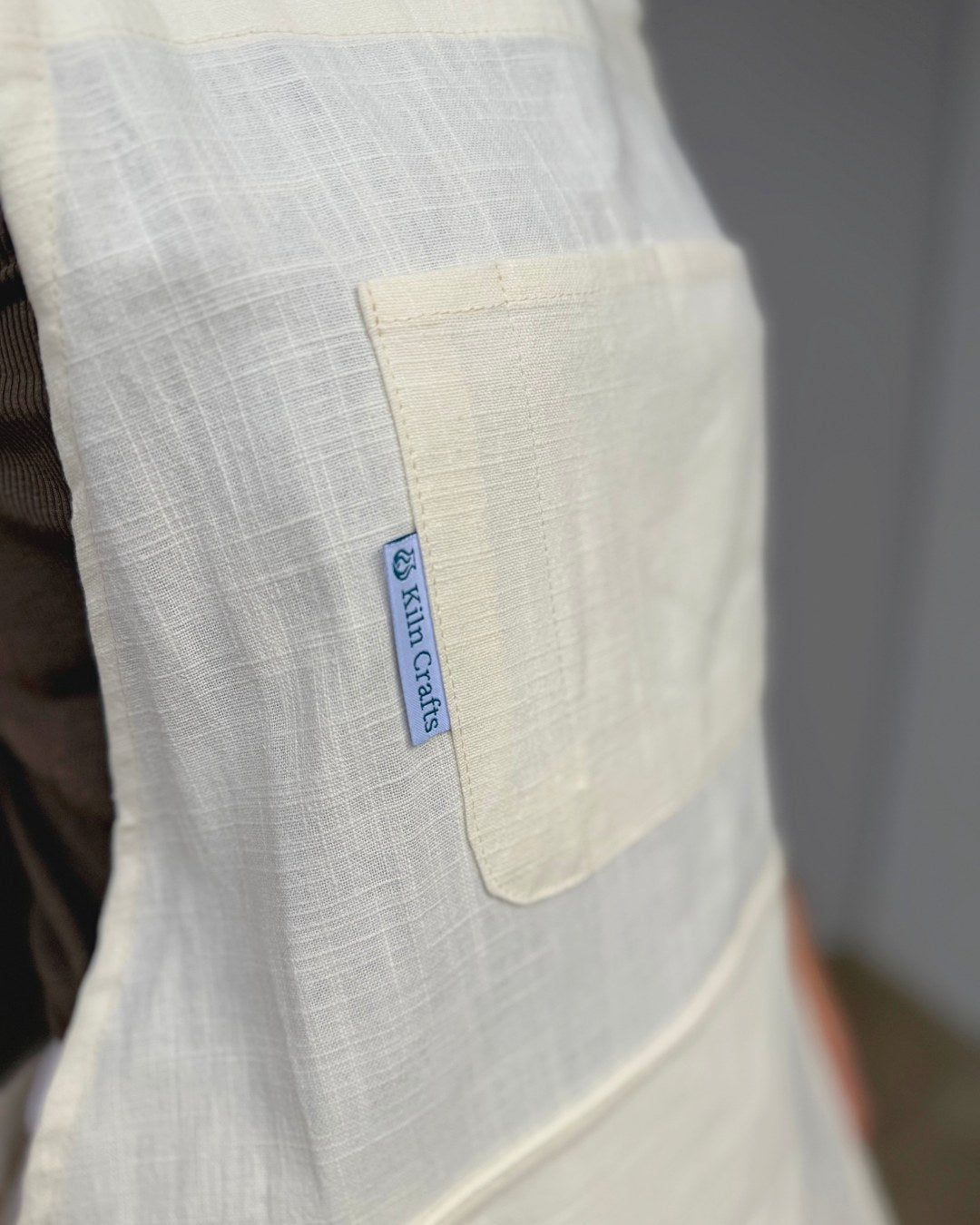 Close-up of the Milk Kiln Crafts Craft Apron chest pocket and woven Kiln Crafts label