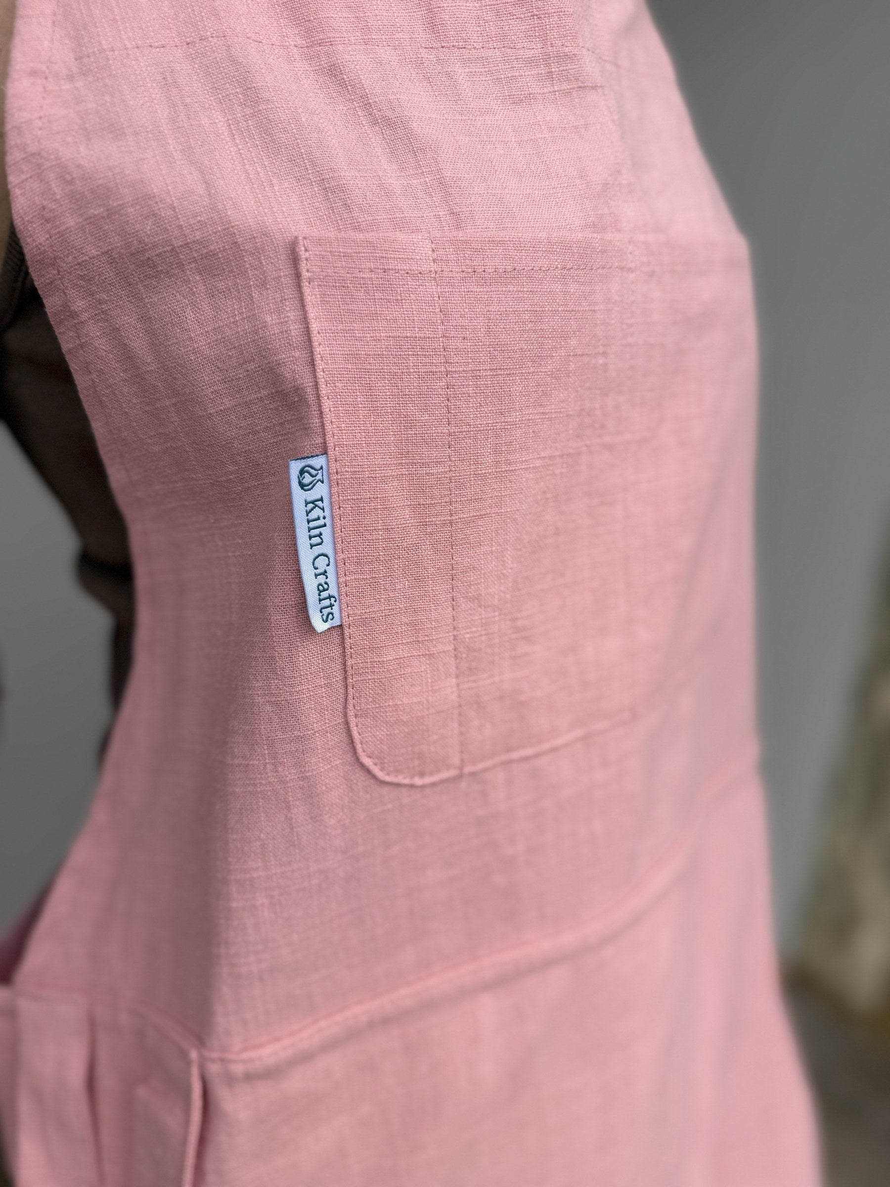 Close-up of the Pink Kiln Crafts Craft Apron chest pocket and woven Kiln Crafts label